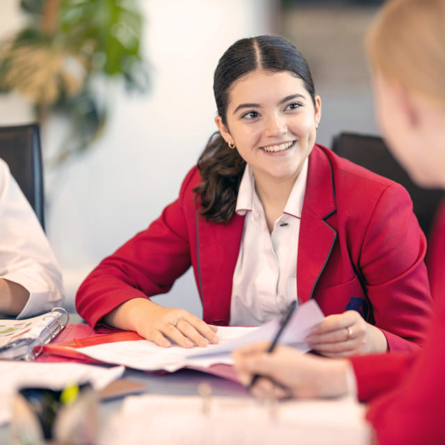 Smiling senior female student in blazer at school desk