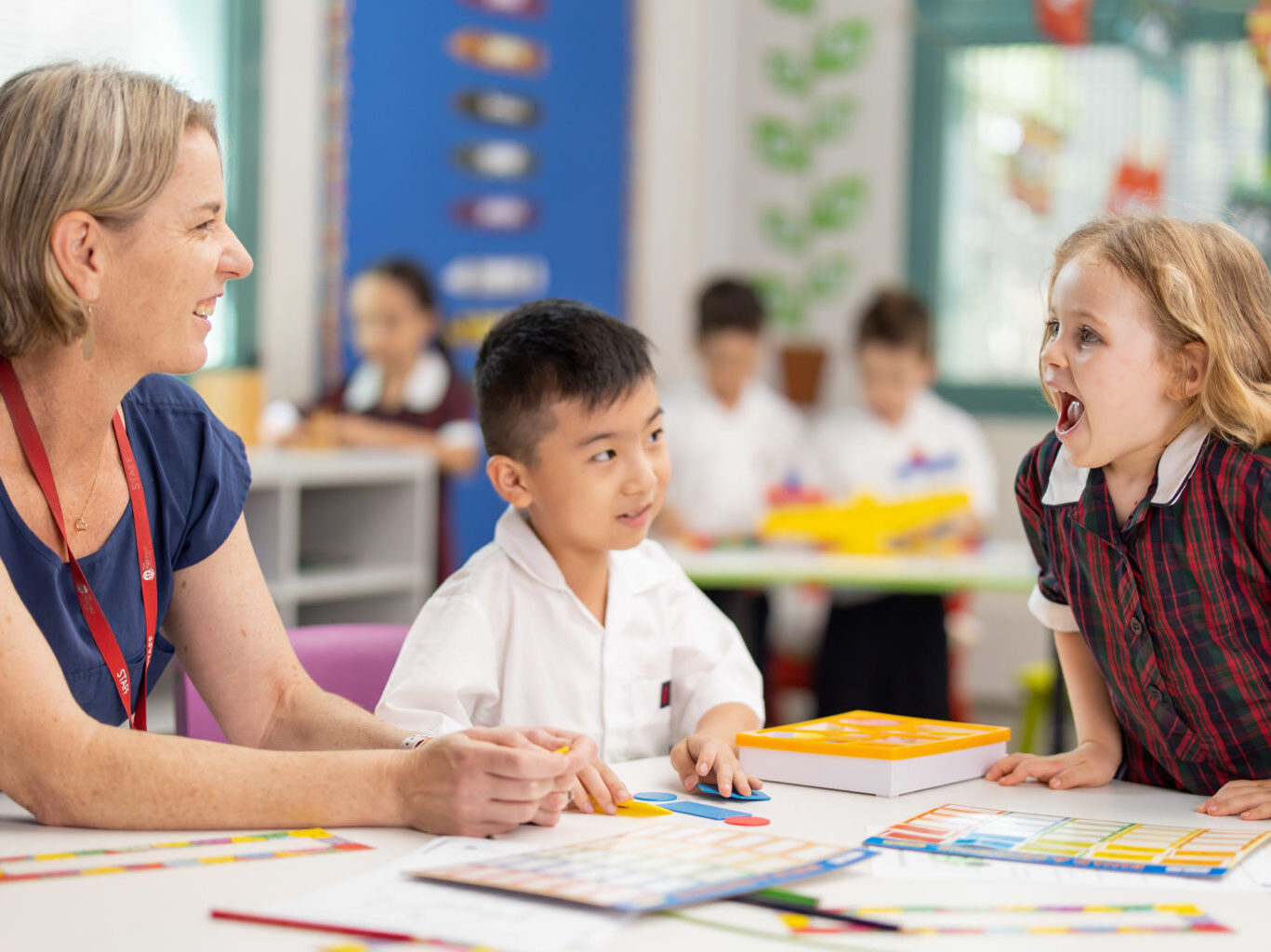 Two infants school children (one male, one female) interact with a school teacher at a desk